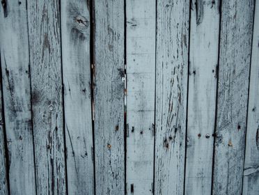 Weathered old fence made of narrow wooden planks of gray color in daylight