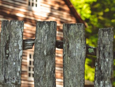Close-up of an old wooden fence with a blurred rustic cabin in the background.