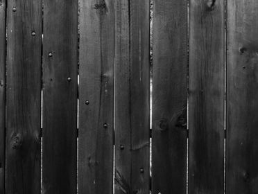 Close-up of a black and white textured wooden fence with visible knots and grain.