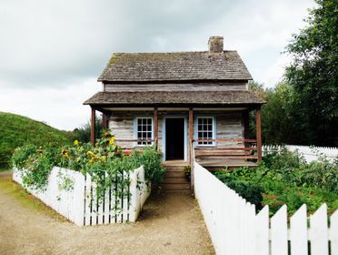 A quaint wooden cabin surrounded by greenery and a white picket fence, embodying rustic charm.