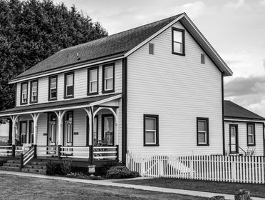 Black and white photo of a classic wooden house with picket fence.