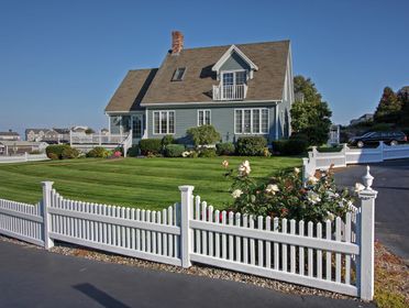 A picturesque New England home with white picket fence and manicured lawn, perfect for residential living.