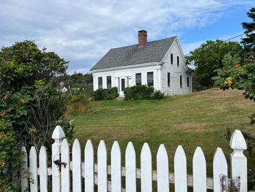 Quaint white cottage with picket fence and lush garden, perfect for a serene coastal retreat.