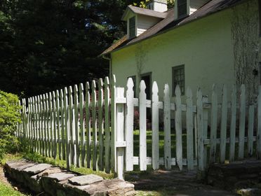 A rustic house in Pennsylvania with a classic white picket fence under a serene summer setting.