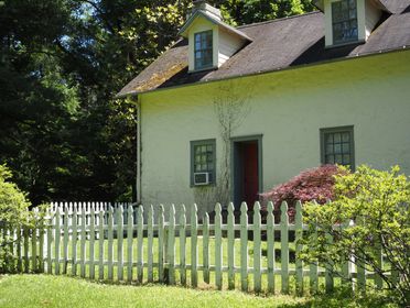 A quaint cottage with a red door and white fence in lush greenery. Ideal for serene home-themed visuals.