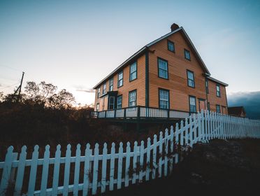 A picturesque wooden house with a white picket fence, captured at twilight, exuding warmth and charm.