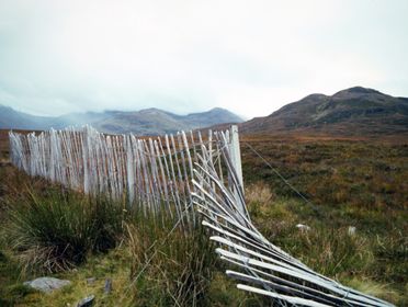Rural landscape in the Scottish Highlands featuring a rustic white wooden fence and rolling hills.