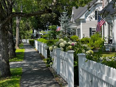 Beautiful suburban street in summer with white picket fences and American flags.