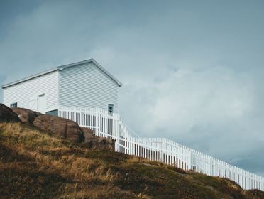 A white house on a rocky hill with a white wooden fence under a cloudy sky.