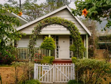 A quaint cottage with lush greenery and a welcoming gate in a garden setting.