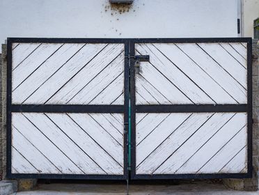 A rustic white wooden gate with diagonal panels and a black metal frame in a residential entrance.