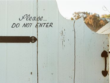 White wooden gate with 'Do Not Enter' sign, sunlit during the day.