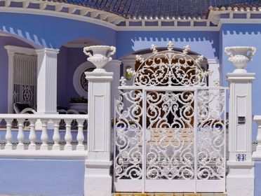 Ornate white iron gate and columns in front of a blue villa in Torrevieja, Spain.