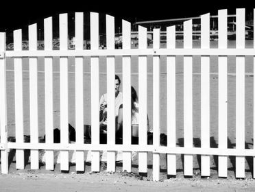 Black and white image of a couple seated on the beach behind a white picket fence in Mar del Plata.