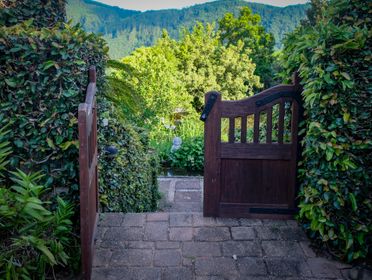 Open wooden gate leading to a lush garden with scenic mountain views.