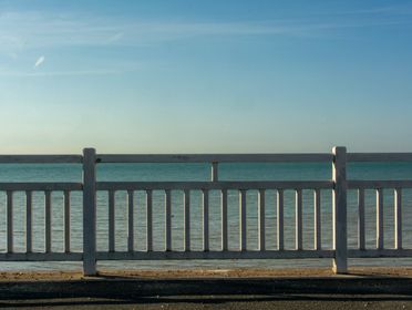Peaceful seascape with a clear sky, viewed through a white wooden fence on a calm day.