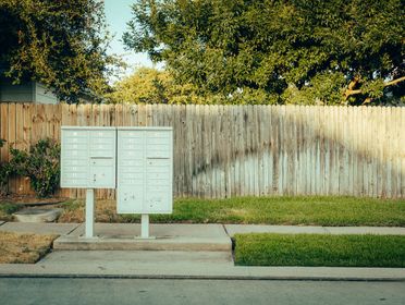 Mailboxes in a suburban area with a wooden fence and trees in the background.