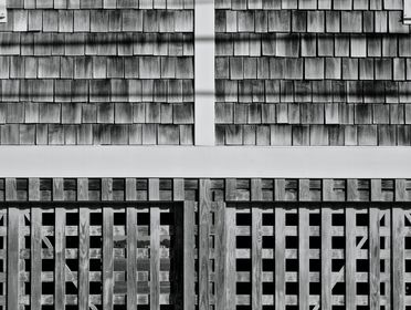 Grayscale photo showcasing a textured wooden wall with shingles and lattice design.