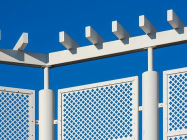 Close-up of a geometric white fence with lattice design against a clear blue sky.