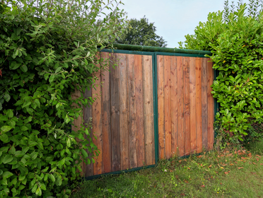 A wooden garden gate framed by vibrant green foliage under a clear sky.