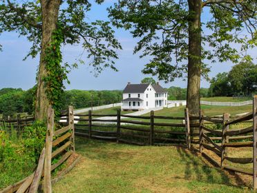 Rustic wooden fence leading to a picturesque white house on a sunny day.