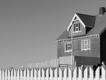 Black and white photo of a wooden house with white picket fence in rural Iceland.