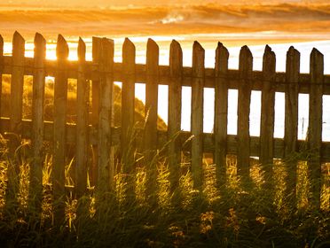 Picturesque view of sunlight streaming through a wooden fence by the beach during golden hour.