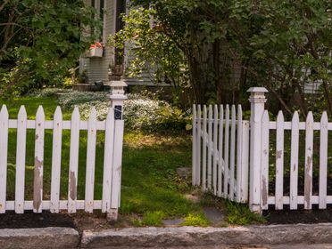 White picket fence in a lush garden setting beside a traditional house.