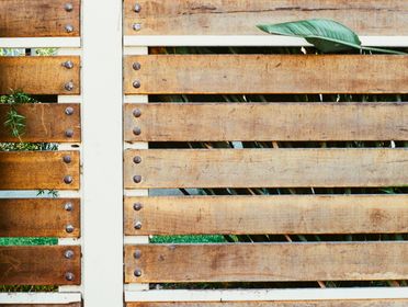 Close-up of a rustic wooden fence with green leaves peeking through the gaps.